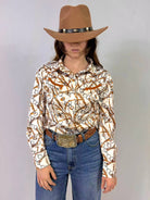 Person wearing a patterned shirt, jeans, and a cowboy hat with a belt on a plain background