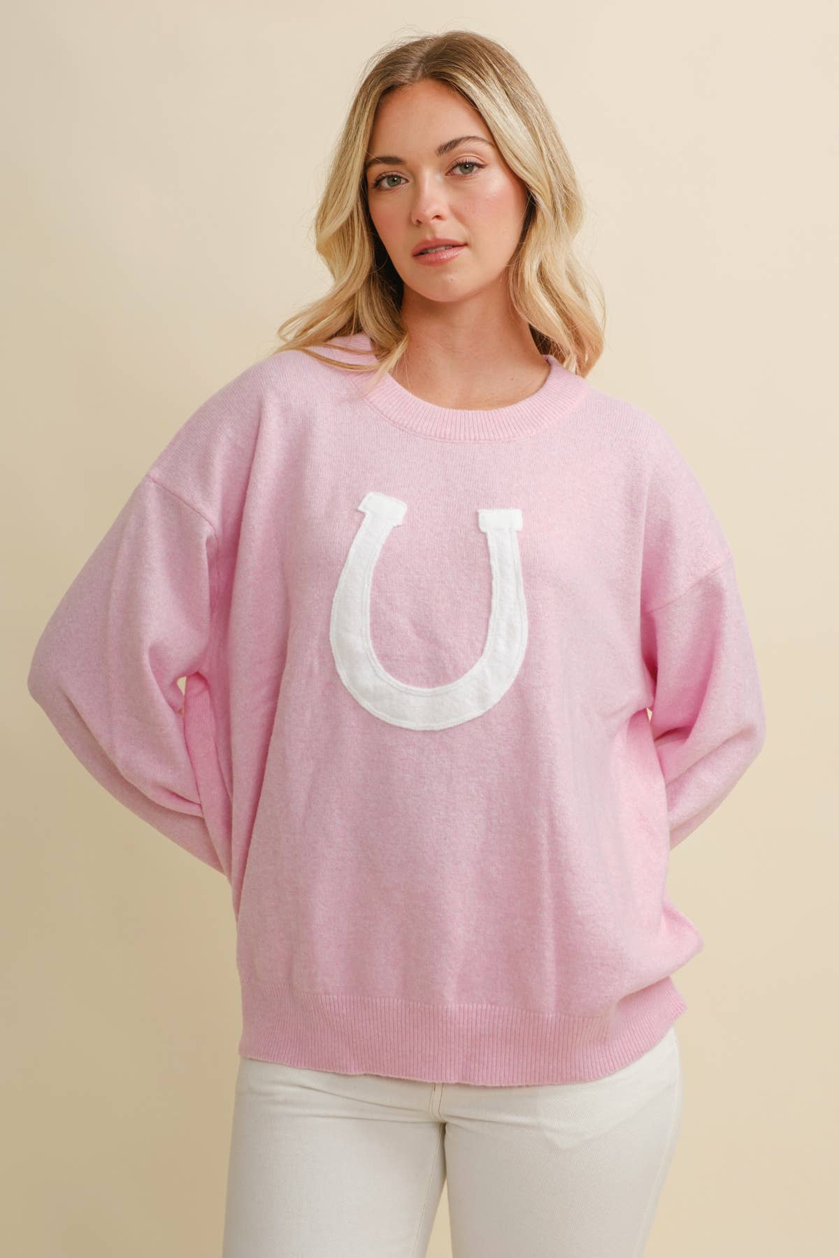 Woman wearing a pink sweater with a white horseshoe design on a beige background