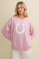 Woman wearing a pink sweater with a white horseshoe design on a beige background