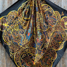 Decorative scarf with intricate gold, blue, and red patterns on a black background.