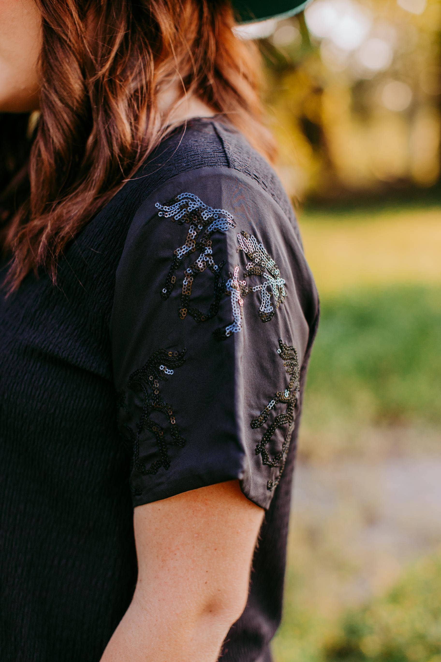 Person wearing a black top with horse sequin on sleeves 