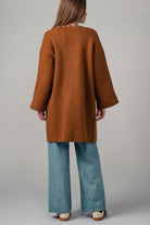 Back view of a woman wearing a brown open coat with white bold stitching  trim 