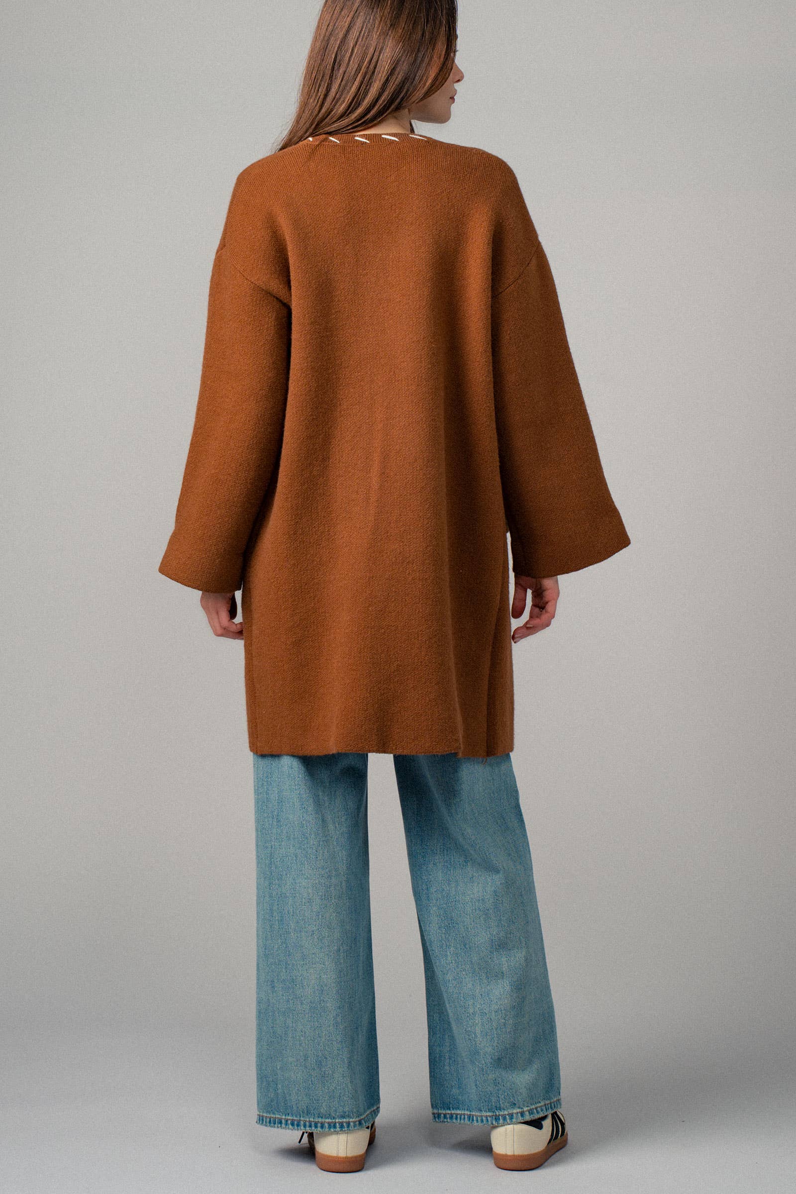 Back view of a woman wearing a brown open coat with white bold stitching  trim 