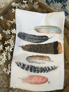 Tea towel with feather designs on a wooden surface with flowers.