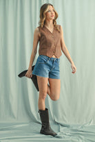 A woman wearing a camel suede button-up vest over a white shirt, paired with Denim Shorts
