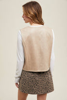 Back of a woman wearing a stone suede snap-up vest over a white shirt, paired with a leopard print mini skirt.