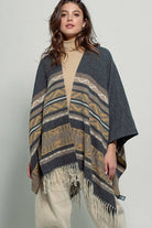 Dark gray poncho with brown and beige striped pattern and fringes on a white background
