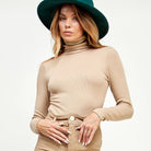 Woman wearing a beige turtleneck and pants with a green hat on a white background