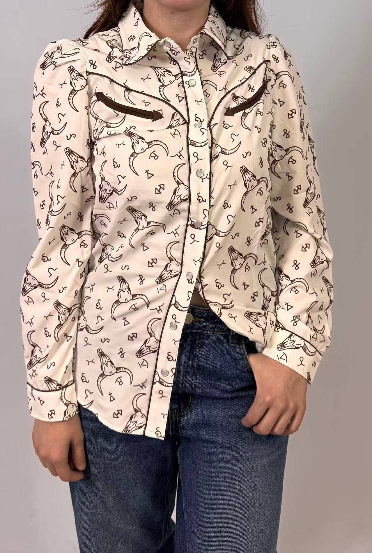 Person wearing a patterned shirt with long sleeves and jeans on a plain background