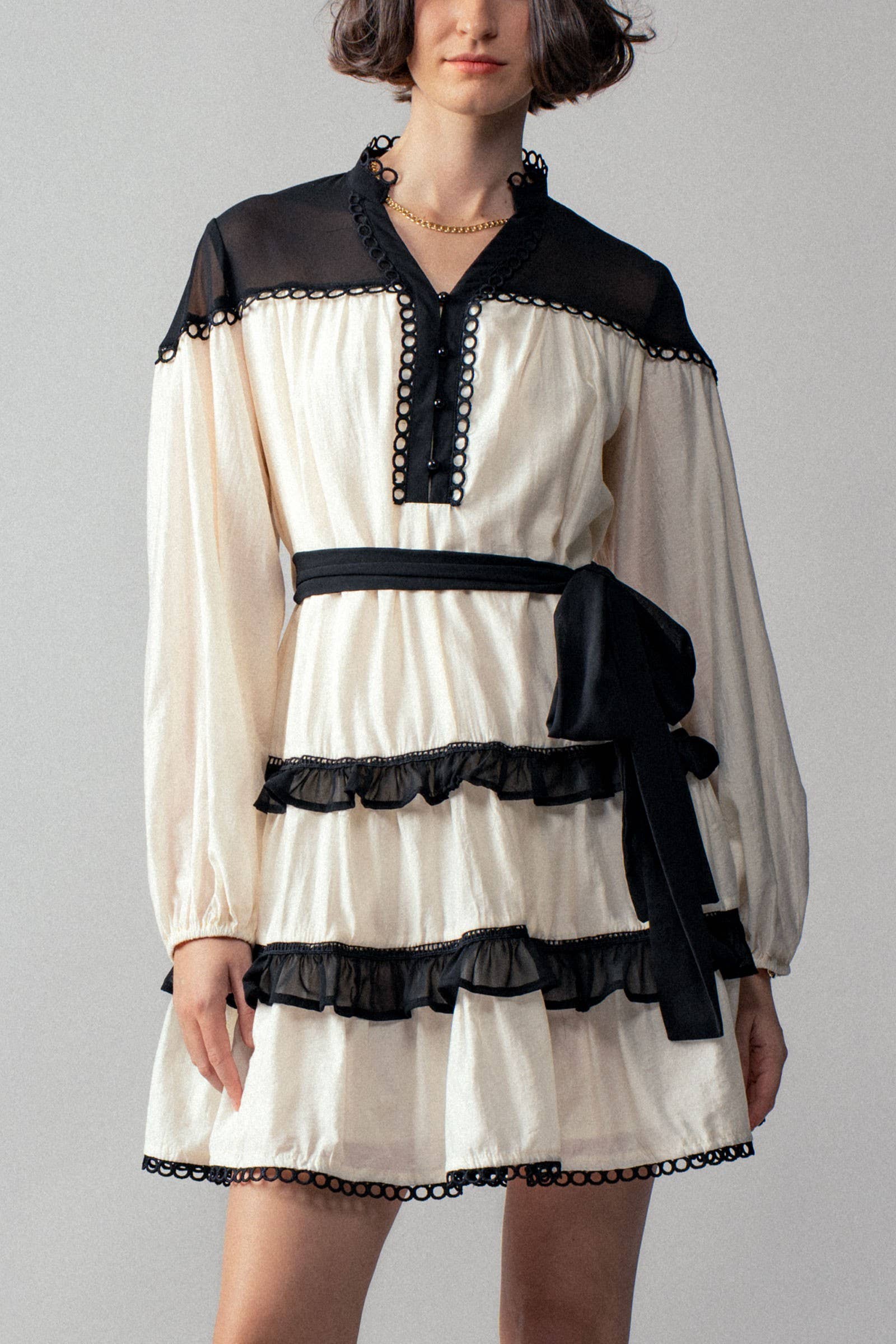 White dress with black ruffle accents worn by a person on a plain background