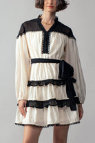 White dress with black ruffle accents worn by a person on a plain background