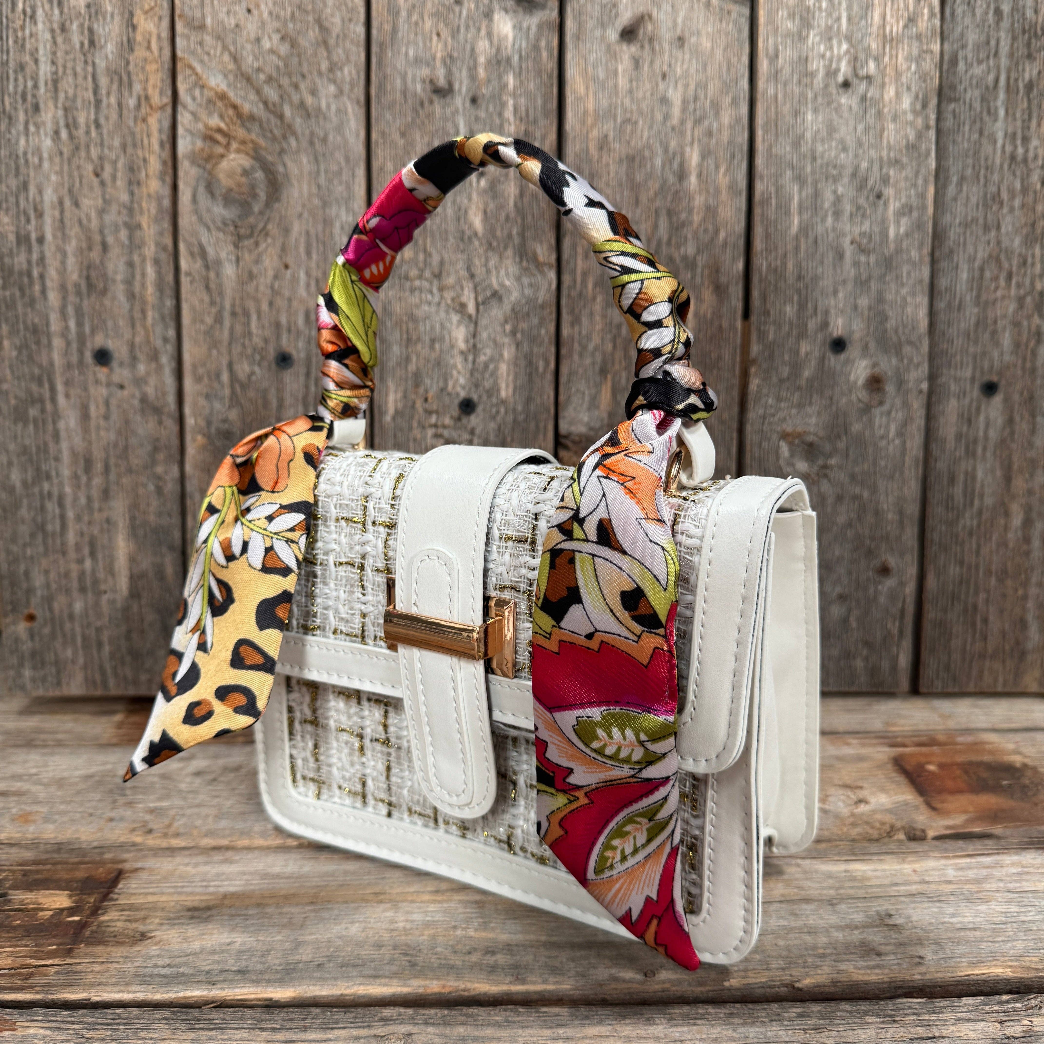 White handbag with a colorful scarf draped over it on a wooden surface