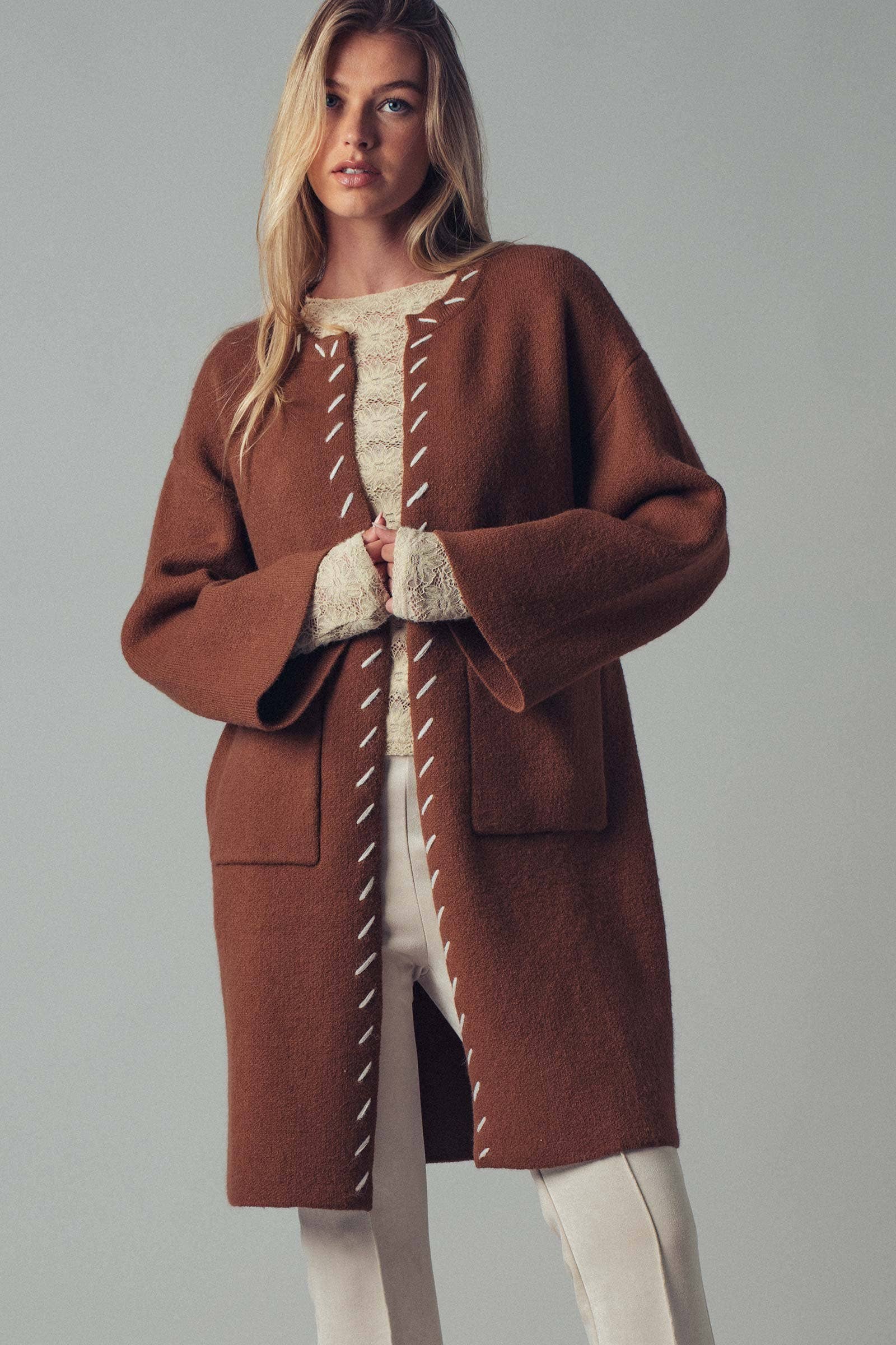 Woman wearing a brown open coat with white bold stitching  trim 