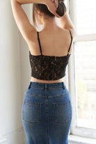 Back of person wearing a black lace top that zips in the back and blue jeans standing by a window.
