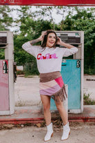 Woman posing in front of a vintage gas pump wearing a 'Cowgirl' sweatshirt.