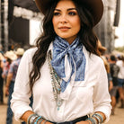 Woman wearing a white shirt, blue bandana, and cowboy hat in a crowd.