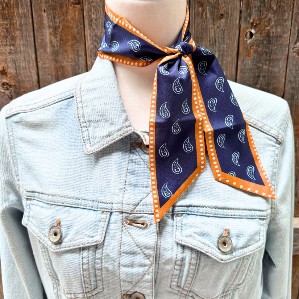 Mannequin wearing a denim jacket with a navy and mustard patterned scarf around its neck against a wooden background.