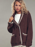 Woman wearing a brown knitted cardigan with white trim on a gray background