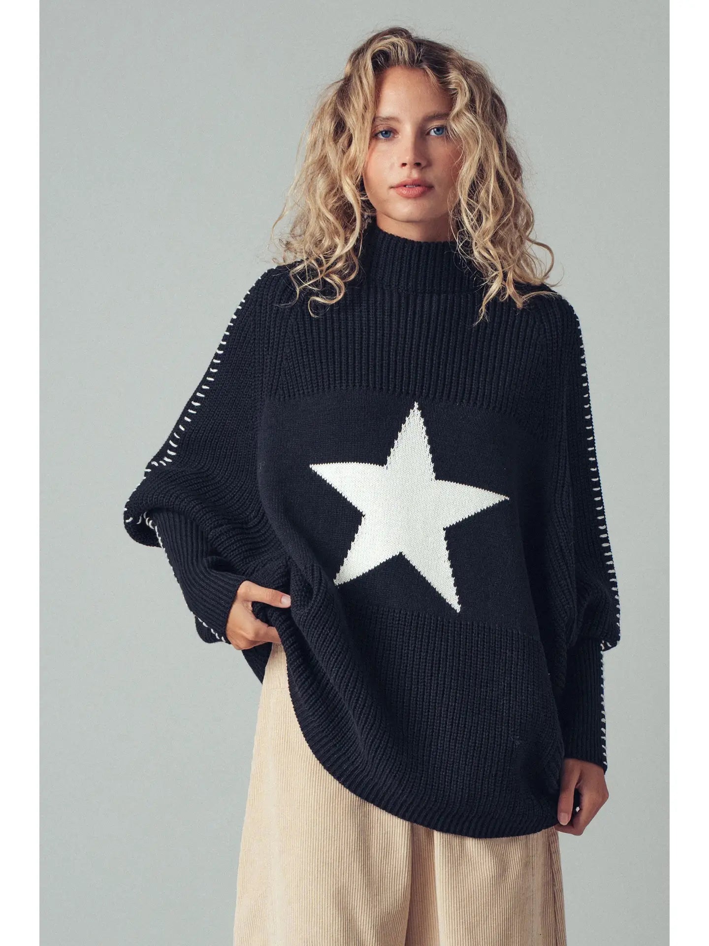 Person wearing a black sweater with a white star design on a plain background