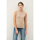 Woman wearing a beige sleeveless top and blue jeans against a white background