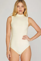 Woman wearing cream sleeveless bodysuit high neck against a plain background