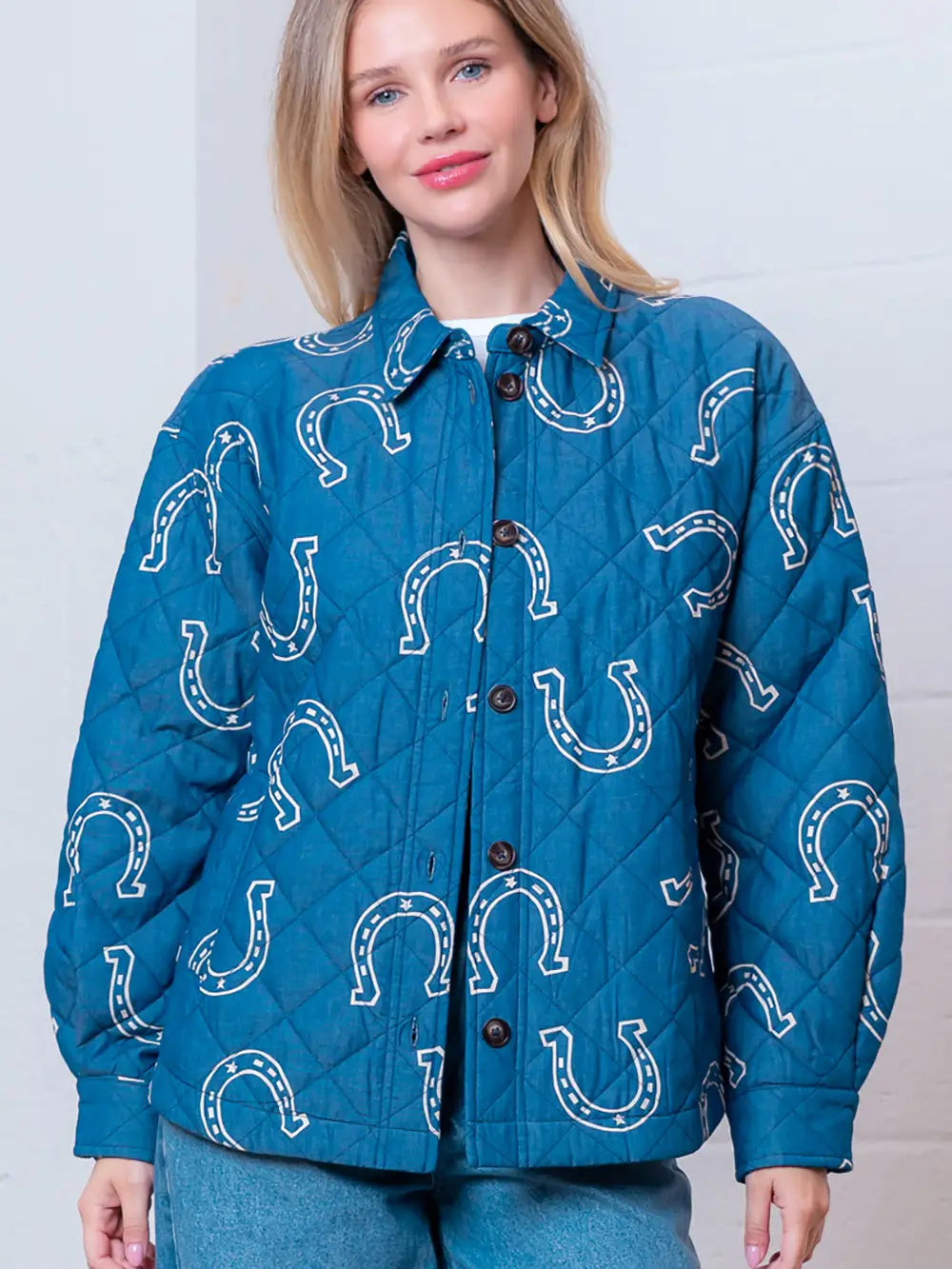 Front view of denim-blue quilted jacket with white horseshoe print and button front on model.