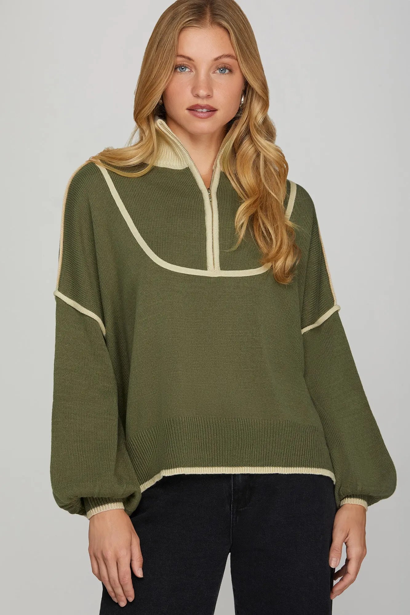 Woman wearing a green sweater with white trim on a plain background