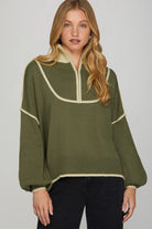 Woman wearing a green sweater with white trim on a plain background
