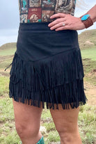 Person wearing a black fringe skirt with a patterned top in an outdoor setting