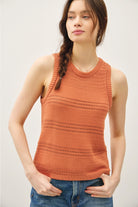 Woman wearing an rust knitted tank top against a plain background