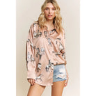 Woman wearing a light champagne shirt with horse print and denim shorts on a beige background