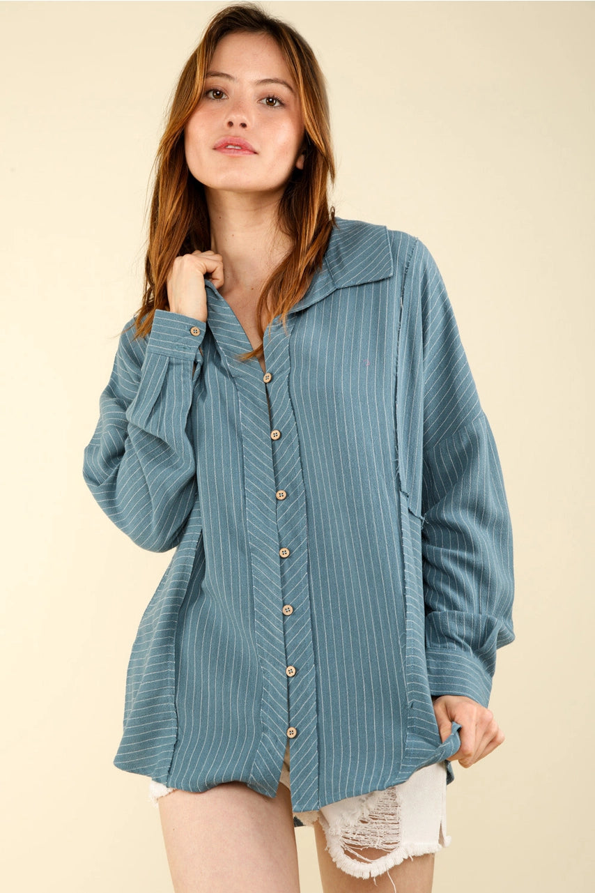 Woman wearing oversized dusty-blue pinstripe button-up collared shirt with drop shoulders and long sleeves; front three-quarter view.”