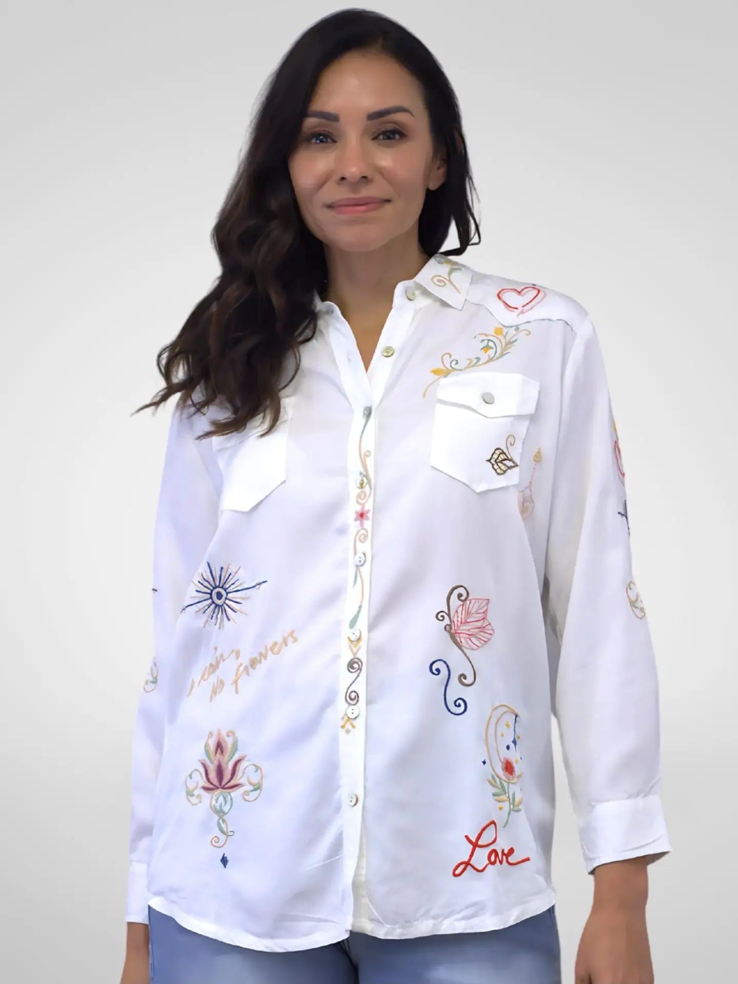 Woman wearing a white embroidered shirt against a plain background