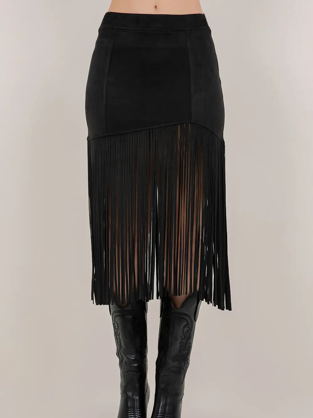 Black fringe skirt worn with black boots on a neutral background