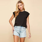 Woman wearing a black sleeveless top and denim shorts on a beige background
