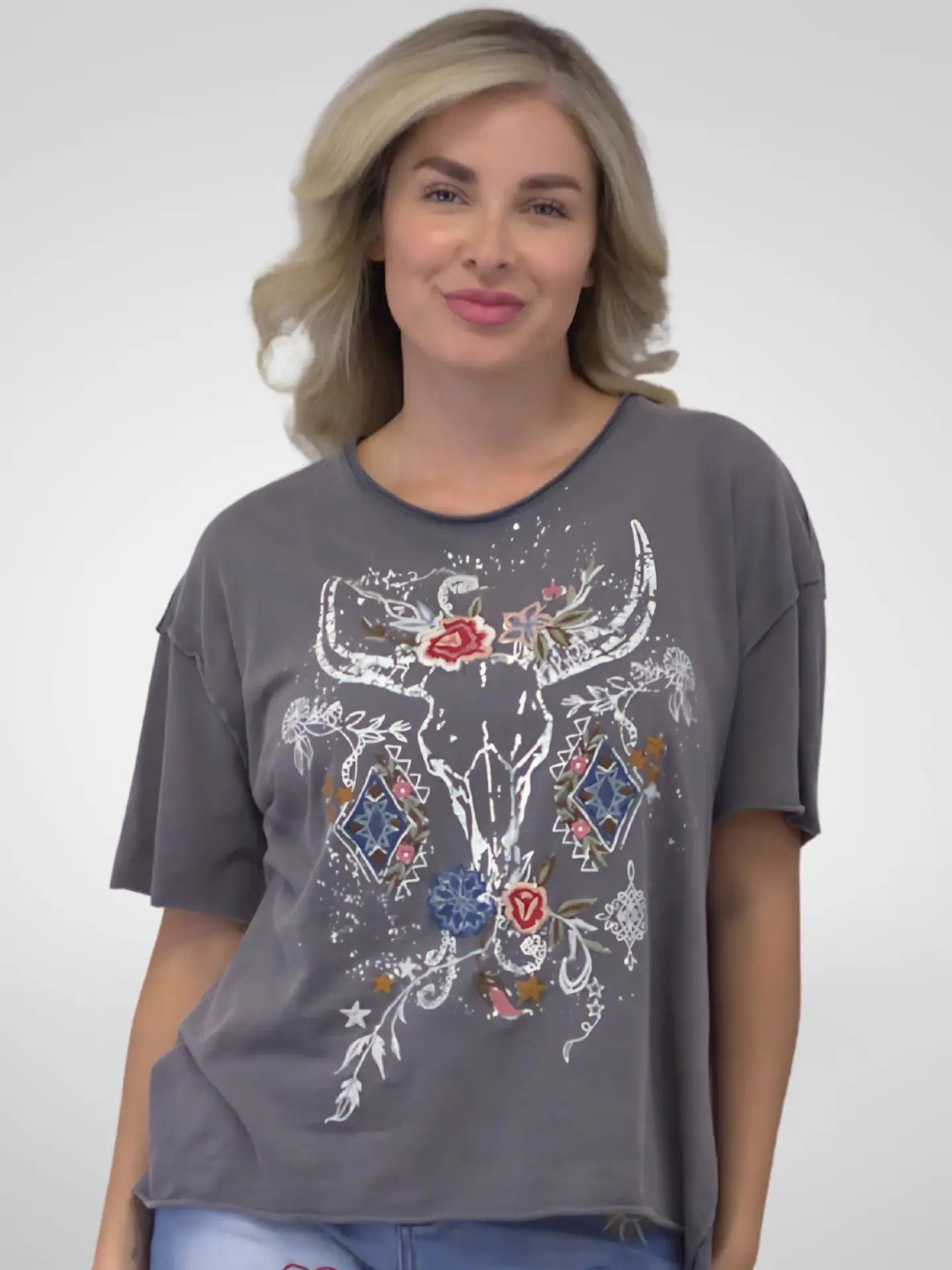 Woman wearing a gray t-shirt with a decorative bull skull design on a plain background