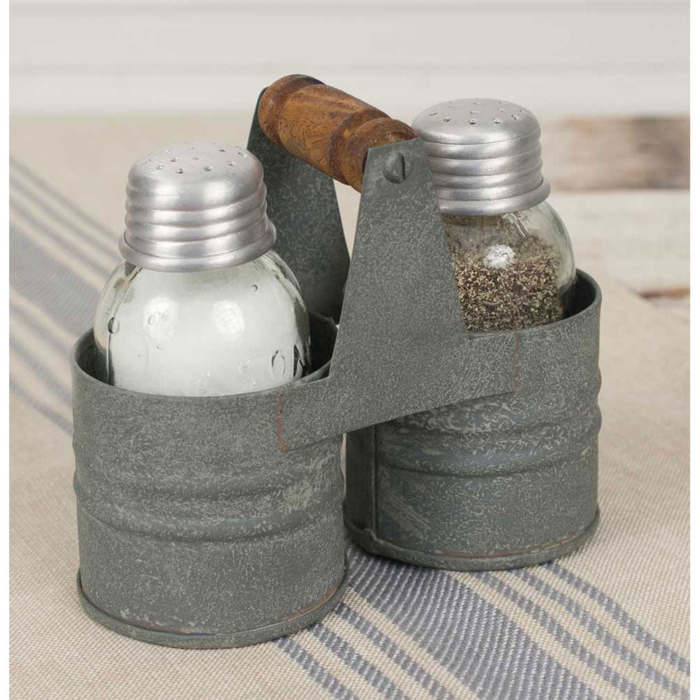 Two salt and pepper shakers in a metal caddy  with a wood handle on a striped surface