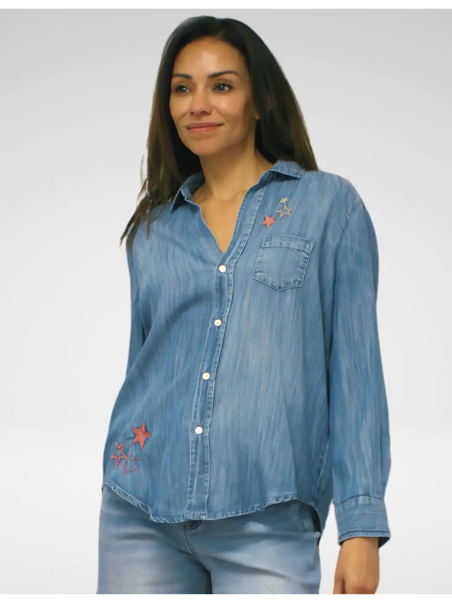 Woman wearing a  long sleeve blue denim shirt with  embroidered star patterns on a plain background