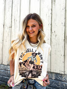 Woman wearing a graphic t-shirt with a design and text, standing against a wooden fence.