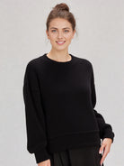 Woman in a black round-neck textured knit oversized top with drop shoulders and long sleeves, relaxed fit.”