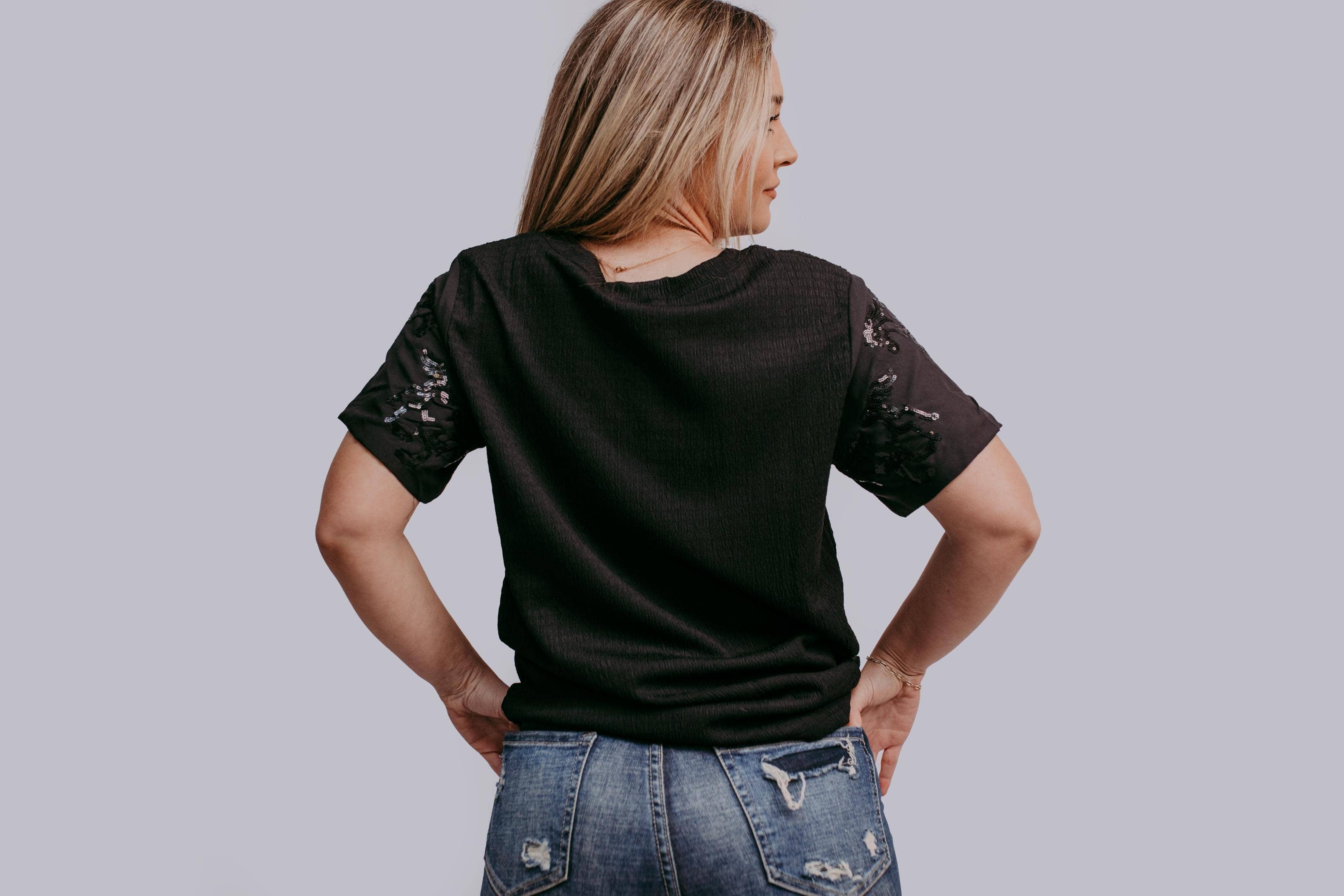 Woman wearing a black t-shirt with horse sequins on a plain background