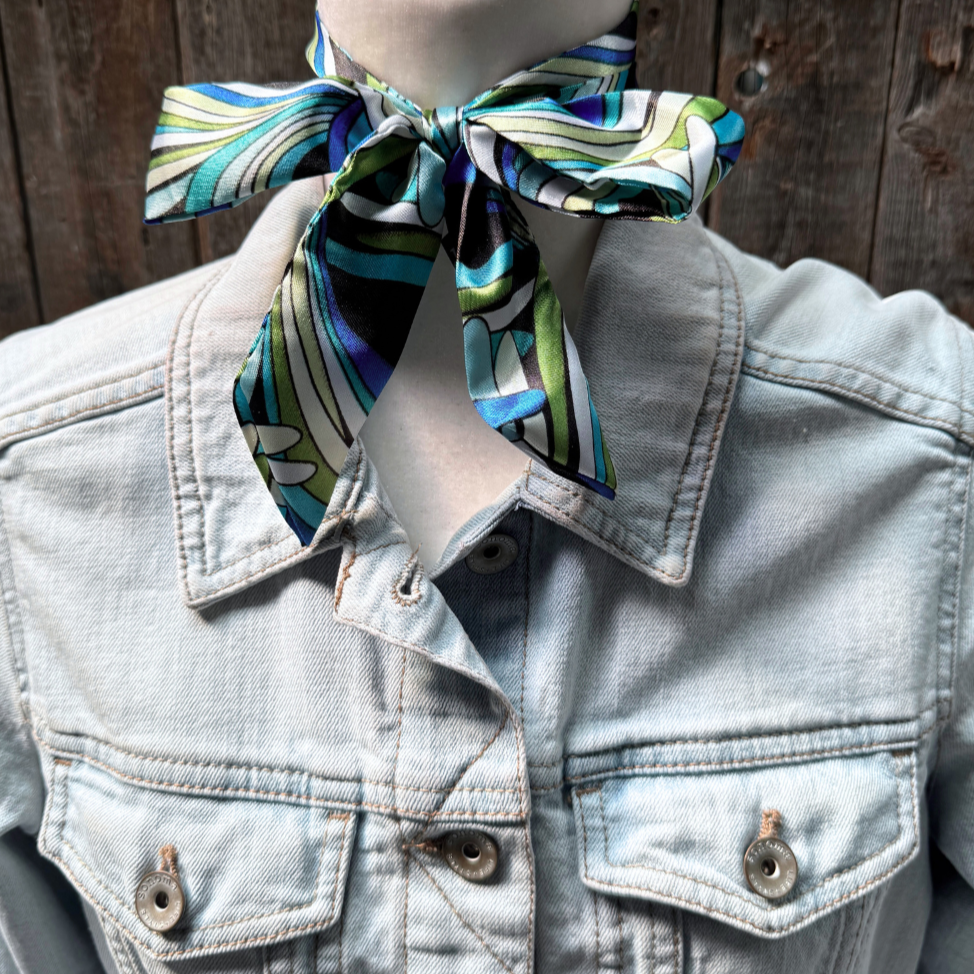 Mannequin wearing a light blue denim jacket with a colorful scarf tied around its neck against a wooden background.