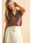 Woman wearing a brown sleeveless blouse and light-colored pants against a beige background