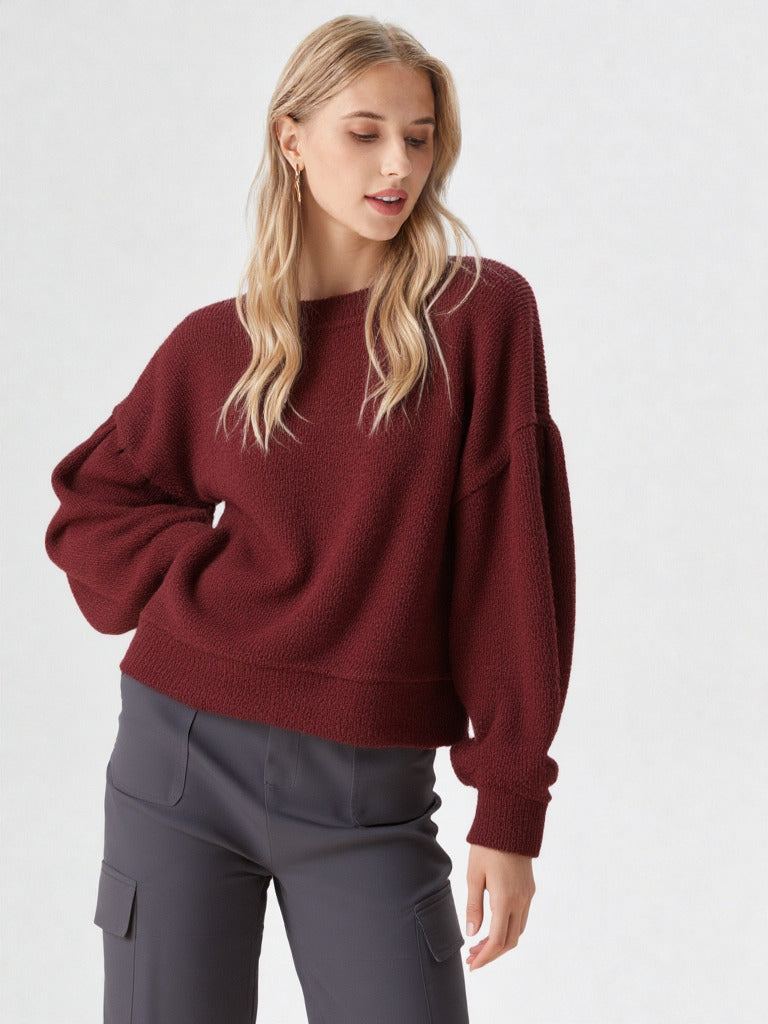Woman in a black round-neck textured knit oversized top with drop shoulders and long sleeves, relaxed fit.”