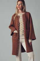 Woman wearing a brown open coat with white bold stitching  trim on a background