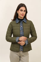 Woman wearing a green puffer jacket with denim collar and cuffs on a beige background