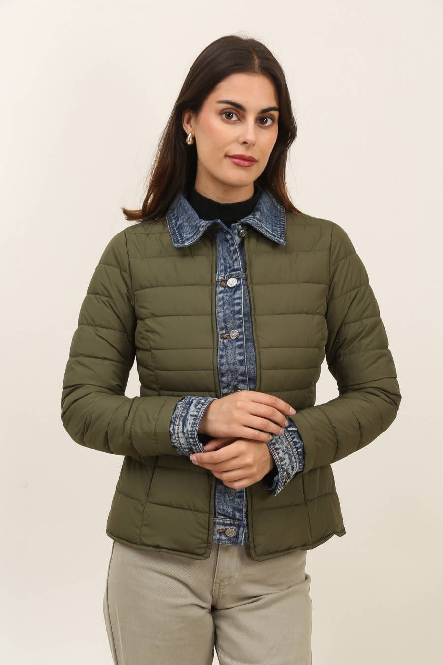 Woman wearing a green puffer jacket with denim collar and cuffs on a beige background