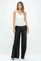 Woman wearing a white sleeveless top and black wide-leg pants on a white background