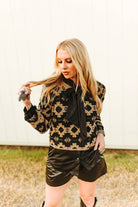 Woman wearing a black and gold patterned jacket with leather shorts outdoors.