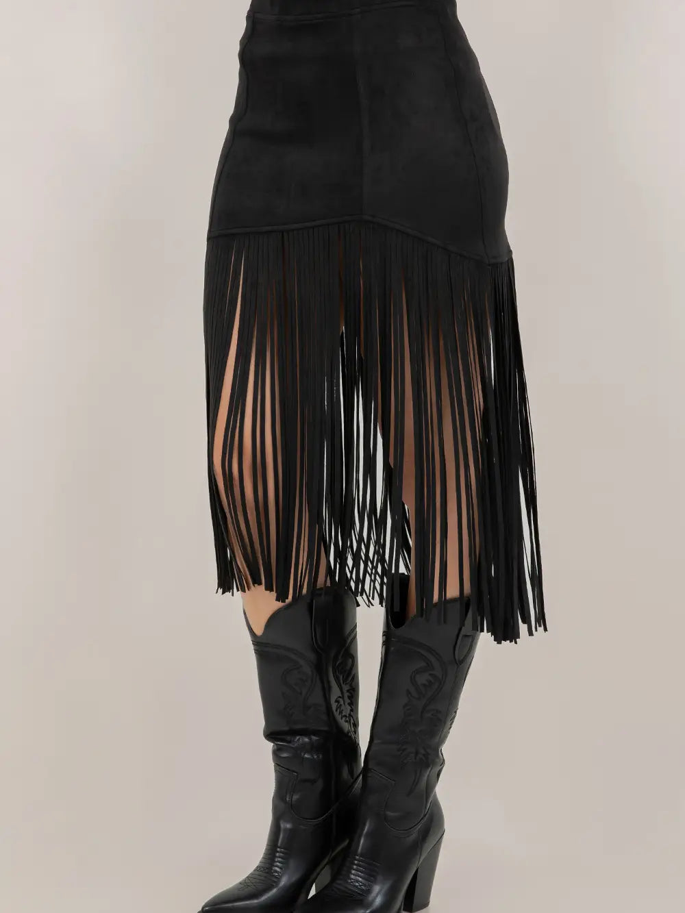 Black fringe skirt with sheer panels worn with black boots on a neutral background